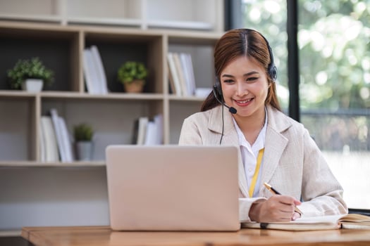 Asian call center with headset and microphone working on her laptop. Female operator provide exceptional customer service. Supportive call center agent helping customer on inquiry. Enthusiastic photo
