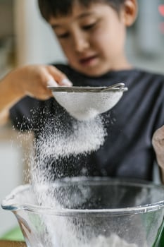 The child cooks in the kitchen. Sifts the flour. photo
