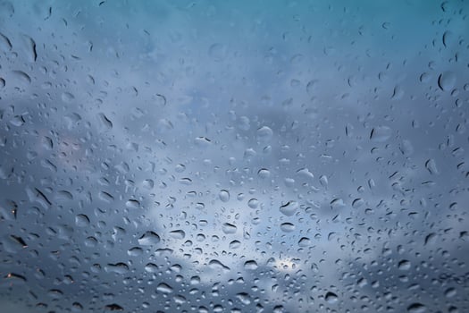 Rain drops on window glass with cloudy sky background. photo