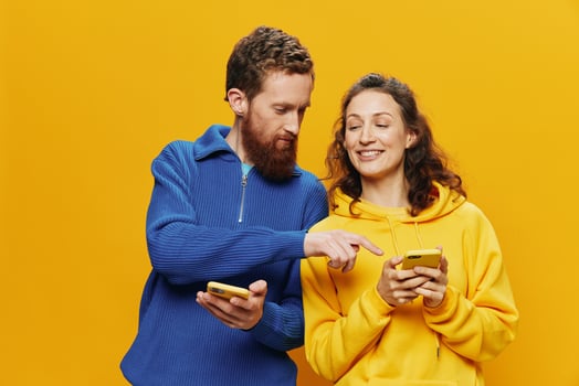Woman man cheerful couple with phones in hand social networking and communication crooked smile fun and fight, in yellow background. The concept of real family relationships, freelancers, work online. photo