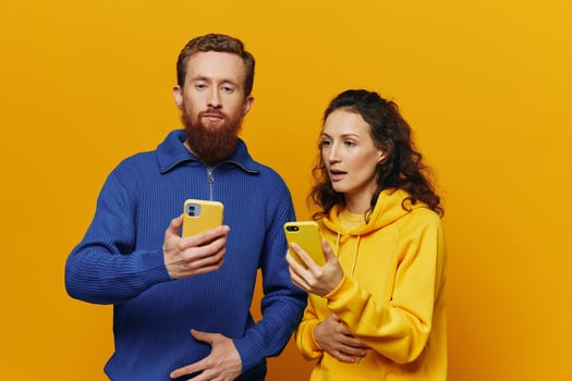 Man and woman couple smiling merrily with phone in hand social media viewing photos and videos, on yellow background, symbols signs and hand gestures, family freelancers.