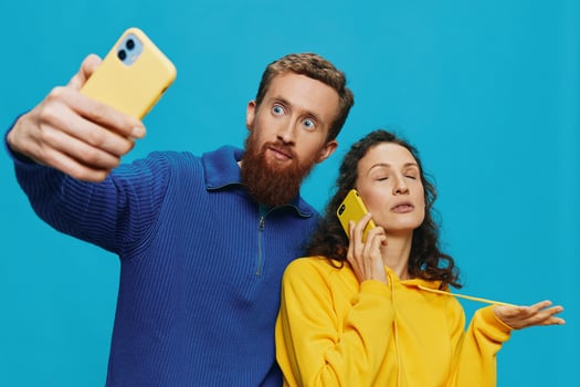 Woman and man funny couple with phones in hand taking selfies crooked smile fun, on blue background. The concept of real family relationships, talking on the phone, work online. photo