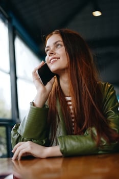 Woman with red hair freelance blogger sitting in a cafe talking on the phone and smiling, hipster girl in trendy clothes lifestyle photo