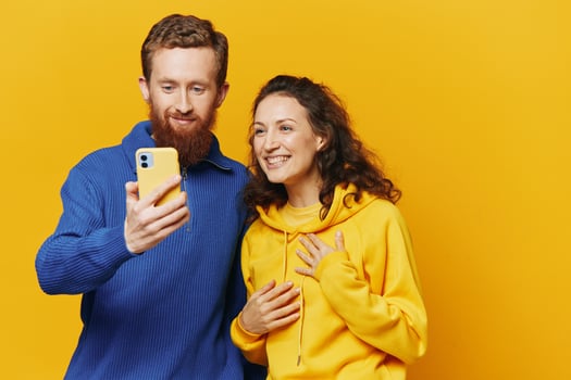 Man and woman couple smiling merrily with phone in hand social media viewing photos and videos, on yellow background, symbols signs and hand gestures, family freelancers.