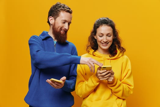 Woman man cheerful couple with phones in hand social networking and communication crooked smile fun and fight, in yellow background. The concept of real family relationships, freelancers, work online. photo