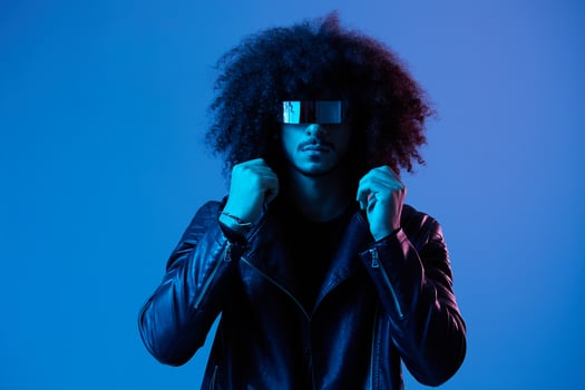 Portrait of fashion man with curly hair with stylish glasses on blue background multinational, colored light, black leather jacket trend, modern concept. photo