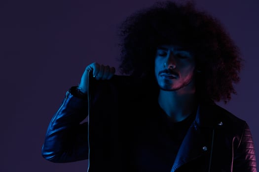 Portrait of fashion man with curly hair on blue background multinational, colored light, black leather jacket trend, modern concept. photo