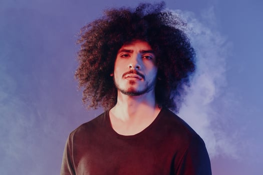 Portrait of a stylish man with curly hair in smoke on a blue background multinational, color light, trend photo