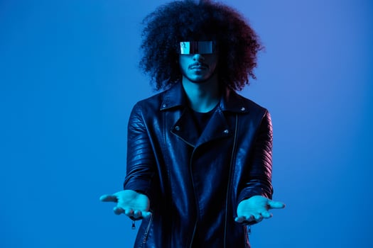Portrait of fashion man with curly hair with stylish glasses on blue background multinational, colored light, black leather jacket trend, modern concept. photo