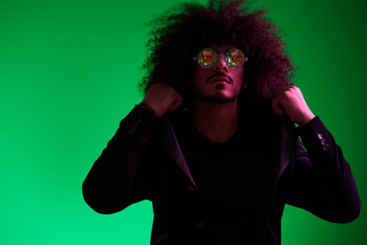 Fashion portrait of a man with curly hair on a green background with sunglasses, multinational, colored pink light, trendy, modern concept. photo