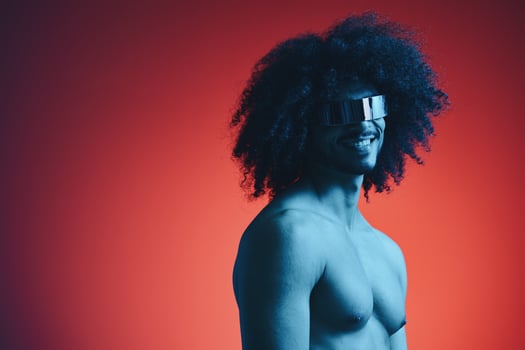 Portrait of fashion man with curly hair on red background with stylish glasses, multinational, colored light, black leather jacket trend, modern concept, sexy body. photo