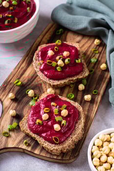 Appetizing rye bread bruschettas with beetroot hummus and chives on a cutting board vertical view photo