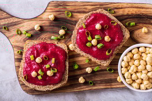 Close up of  rye bread sandwiches with beetroot hummus and herbs on a cutting board top view photo