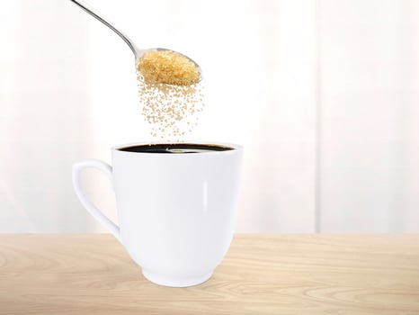 Spoon pour sugar into a coffee mug on the wooden floor inside the room. photo