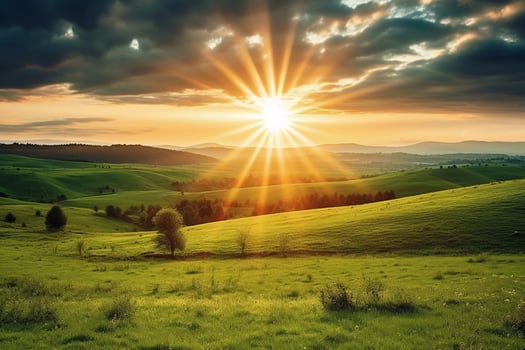 The sun rises over a hillside with grassy fields and an area with a hill. photo