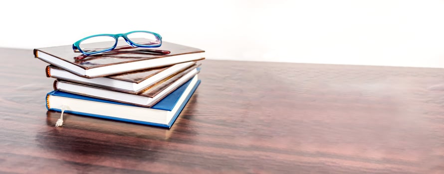 Stack of books with reading glasses on wooden desk. Education banner. photo
