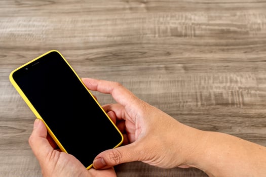 Female hand holding cell phone on wooden table. photo