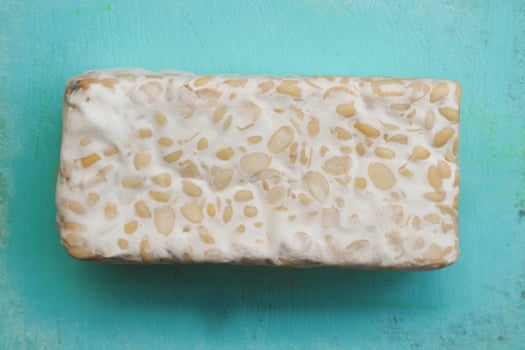 Fresh raw tempeh, on a plastic cutting board on a wooden background. Food preparation concept photo