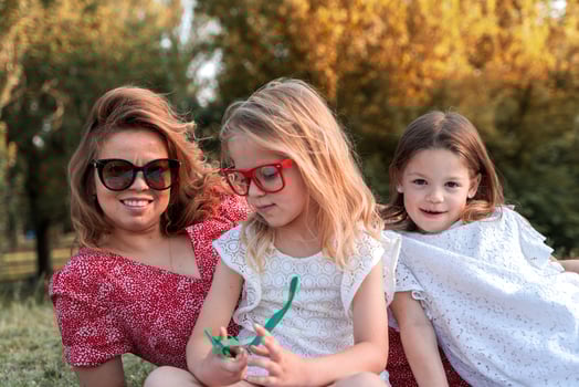 portrait of mom with cute daughters have fun sitting on grass in the park photo