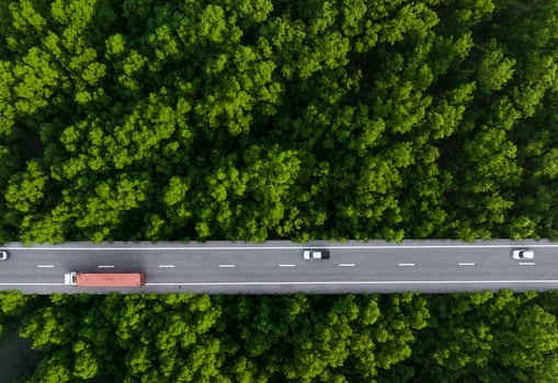 Aerial top view of car and truck driving on highway road in green forest. Sustainable transport. Drone view of hydrogen energy truck and electric vehicle driving on asphalt road through green forest. photo
