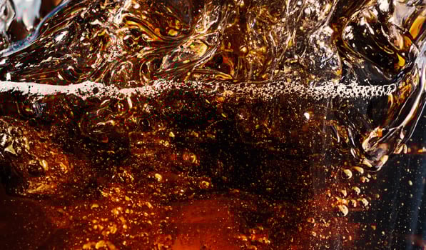 Cola with Ice. Close up of the ice cubes in cola water. Texture of carbonate drink with bubbles in glass. Cola soda and ice splashing fizzing or floating up to top of surface. Cold drink background. photo