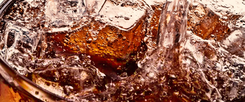 Splashing of Cola and Ice. Cola soda and ice splashing fizzing or floating up to top of surface. Close up of ice in cola water. Texture of carbonate drink with bubbles in glass. Cold drink background photo