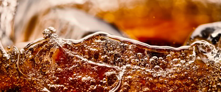 Splashing of Cola and Ice. Cola soda and ice splashing fizzing or floating up to top of surface. Close up of ice in cola water. Texture of carbonate drink with bubbles in glass. Cold drink background photo