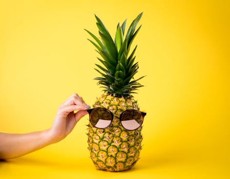 Juicy pineapple with sunglasses, summer vacation concept, female hand, yellow background - nutritious fruit. photo