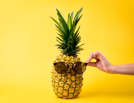 Young woman hand holding sunglasses, nutritious pineapple, vacation travel concept - yellow background photo