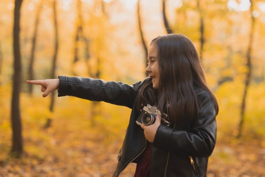 A little girl take a photo with old retro camera in autumn nature. Leisure and hobby concept.