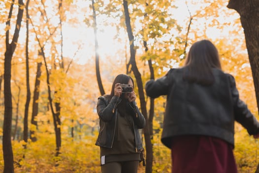 Mother photographer takes pictures of a her daughter in the park in autumn. Hobbies, photo art and leisure concept.