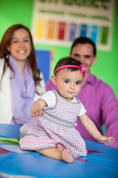 Beautiful ten months baby girl playing with her parents on background. Early stimulation for toddlers concept. photo