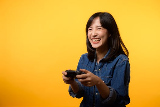 Portrait young asian woman with happy success smile wearing denim clothes holding joystick controller and playing video game. Fun and relax hobby entertainment lifestyle concept. photo