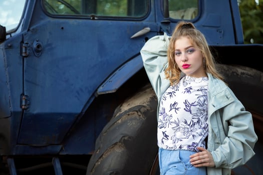 A beautiful country girl in the style of the 90s in bright clothes stands near a tractor. photo