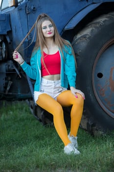 A beautiful country girl in the style of the 90s in bright clothes stands near a tractor. photo