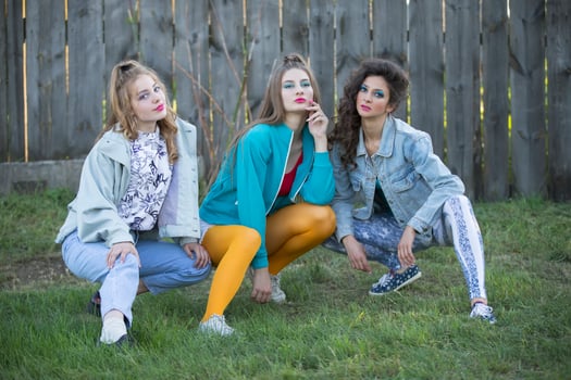 Funny girls in the style of the 90s in bright clothes are sitting near a wooden fence. photo