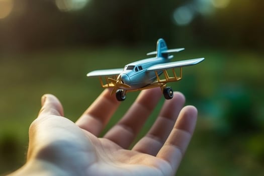close up photo of male hand holding toy airplane against blue sky . image is retro filtered