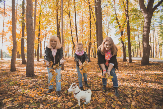Grandmother and mother with granddaughter throw up fall leaves in autumn park and having fun. Generation, leisure and family concept. photo