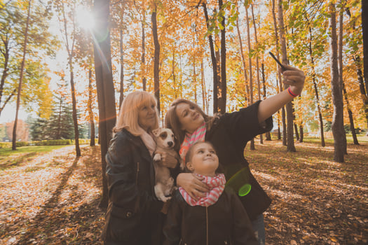 Mother, grandmother and little granddaughter with jack russell terrier dog taking selfie by smartphone outdoors in autumn nature. Family, pets and generation concept photo