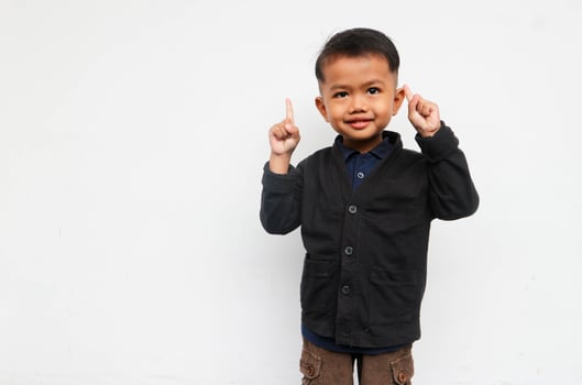 A smiling toddler boy looks at the camera raising his hands and pointing up, isolated on white background photo