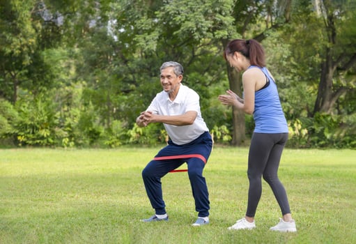 young woman trainer teaching a senior man doing exercise with elastic band,smiling woman applauding beside him,legs stretch exercise for rehabilitation muscles in older adult,concept of elderly health photo