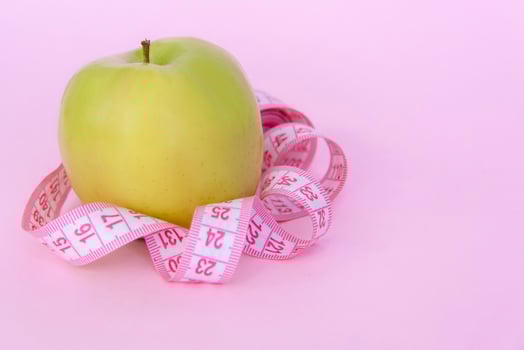 A green apple and a centimeter measuring tape on a pink background. Sports, sports nutrition, healthy eating, diet. Space for the text. photo