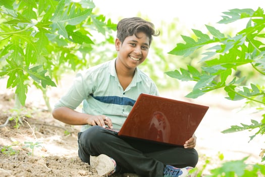 Indian boy studying in farm, holding laptop in hand , poor indian kids photo