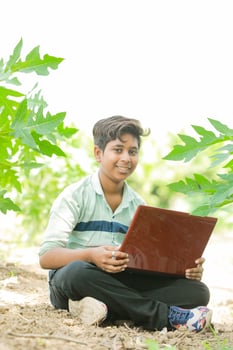 Indian boy studying in farm, holding laptop in hand , poor indian kids photo