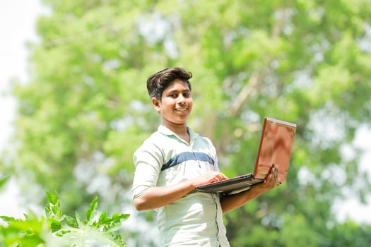 Indian boy studying in farm, holding laptop in hand , poor indian kids photo