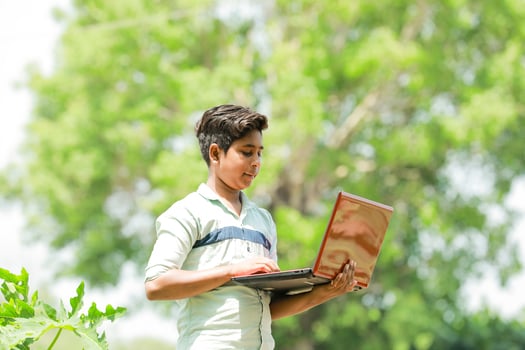 Indian boy studying in farm, holding laptop in hand , poor indian kids photo