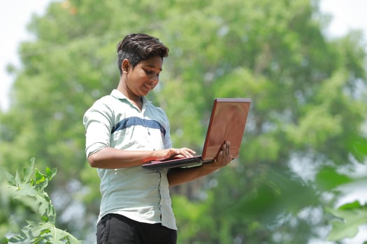 Indian boy studying in farm, holding laptop in hand , poor indian kids photo