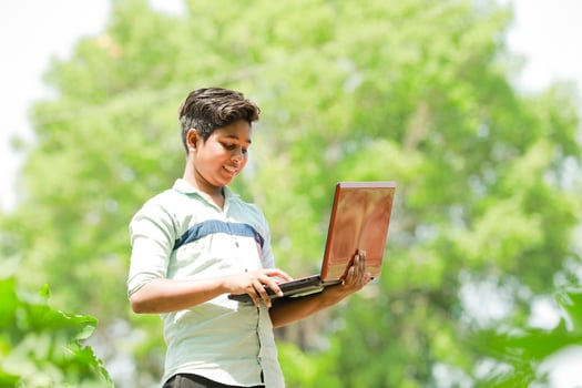 Indian boy studying in farm, holding laptop in hand , poor indian kids photo