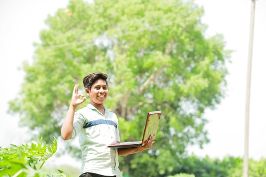 Indian boy studying in farm, holding laptop in hand , poor indian kids photo