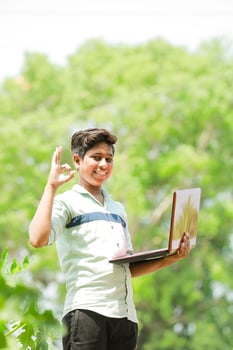 Indian boy studying in farm, holding laptop in hand , poor indian kids photo